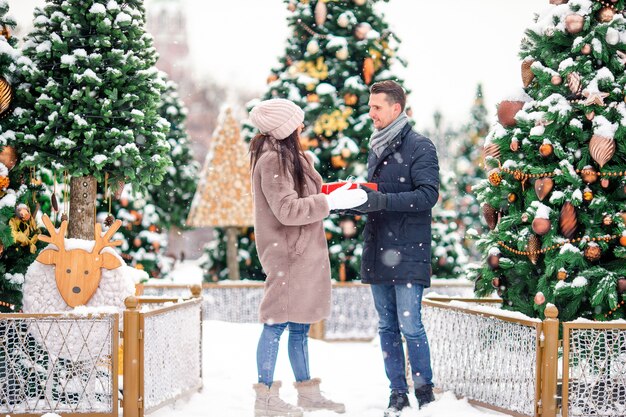 Jeune beau couple gai, fêtant Noël dans la rue et offrant en cadeau.