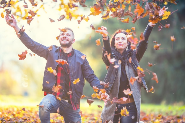 Jeune beau couple heureux - amoureux volant avec des feuilles dans le parc en automne.