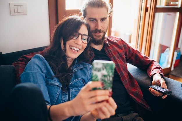 Jeune beau couple heureux assis canapé intérieur maison prenant selfie