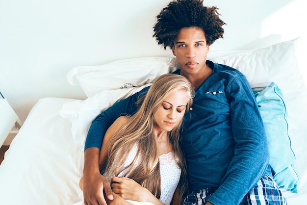 Jeune beau couple interracial détendu allongé dans son lit câlins