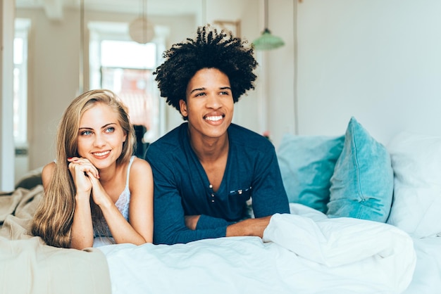 Jeune beau couple interracial détendu allongé dans son lit câlins