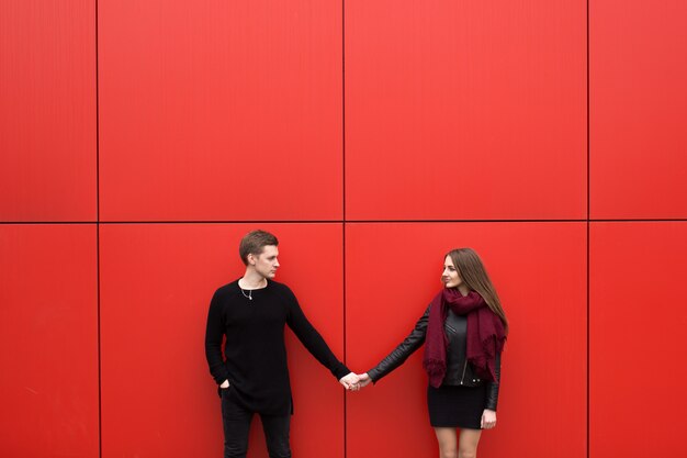 Jeune beau couple posant sur un mur rouge