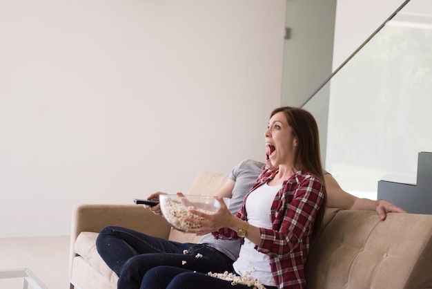 jeune beau couple profitant du temps libre à regarder la télévision avec du pop-corn dans leur villa de luxe