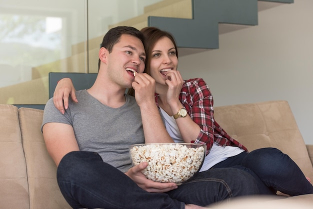 jeune beau couple profitant du temps libre à regarder la télévision avec du pop-corn dans leur villa de luxe