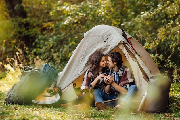 Jeune beau couple en tenue décontractée assis dans un camping près de la tente