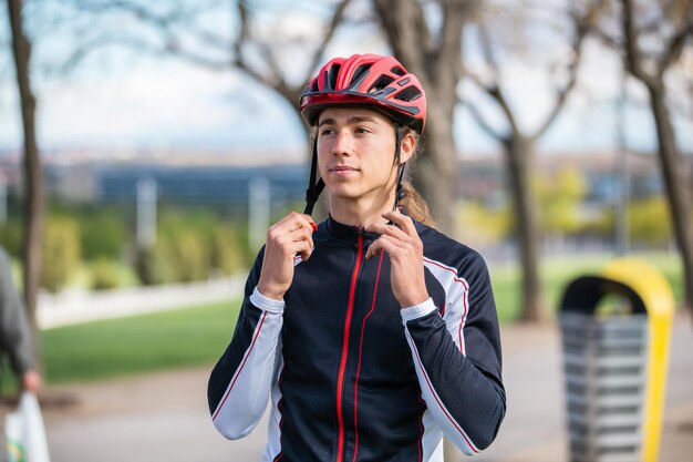 Jeune beau cycliste masculin en tenue de sport bouclant un casque de protection dans un magnifique parc de la ville