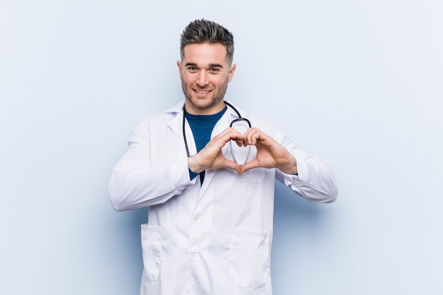 Jeune beau docteur homme souriant et montrant une forme de coeur avec les mains.