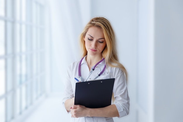 Jeune beau docteur en médecine rédigeant une ordonnance en clinique. Une jolie infirmière tient un stylo à main avec un stéthoscope autour du cou.