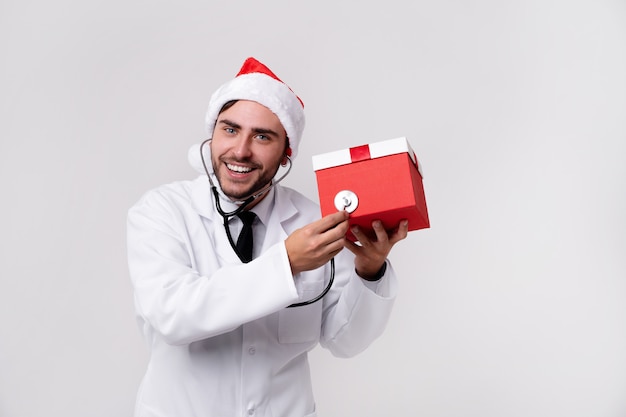 Jeune beau docteur en uniforme blanc et chapeau de père Noël avec cadeau