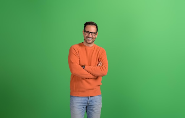 Jeune et beau entrepreneur debout avec les bras croisés et souriant à la caméra sur un fond vert