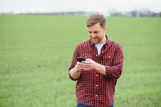 Jeune beau fermier marchant sur les terres agricoles et parlant au téléphone portable