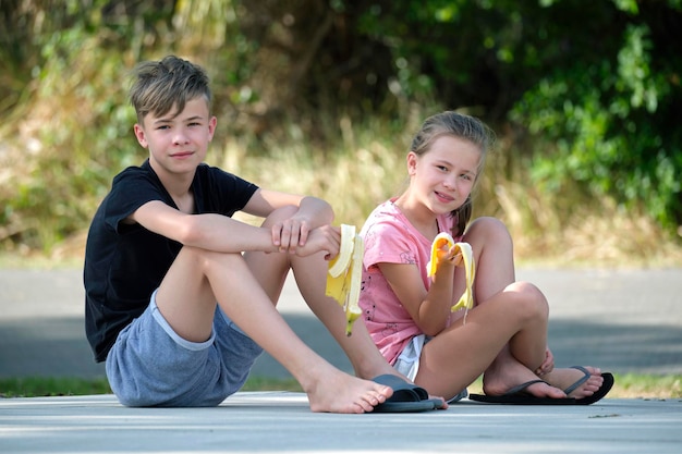 Jeune beau garçon adolescent et jolie fille mangeant une banane mûre savoureuse en train de grignoter à l'extérieur le jour d'été