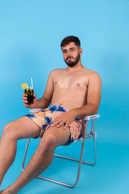 Jeune beau garçon profitant des vacances d'été en buvant du soda au cola froid L'homme est en vacances assis sur la chaise de plage en prenant un verre