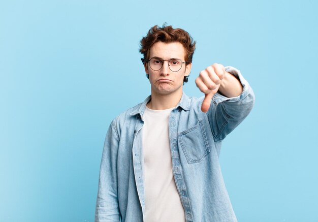 Jeune beau garçon se sentant en colère ennuyé déçu ou mécontent montrant les pouces vers le bas avec un regard sérieux