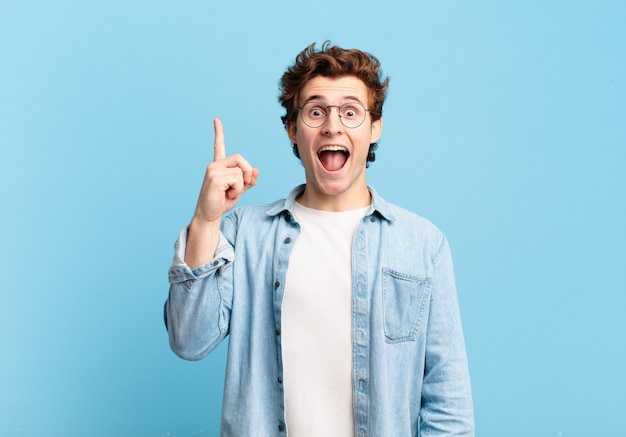 Jeune beau garçon se sentant comme un génie heureux et excité après avoir réalisé une idée, levant joyeusement le doigt, eurêka !