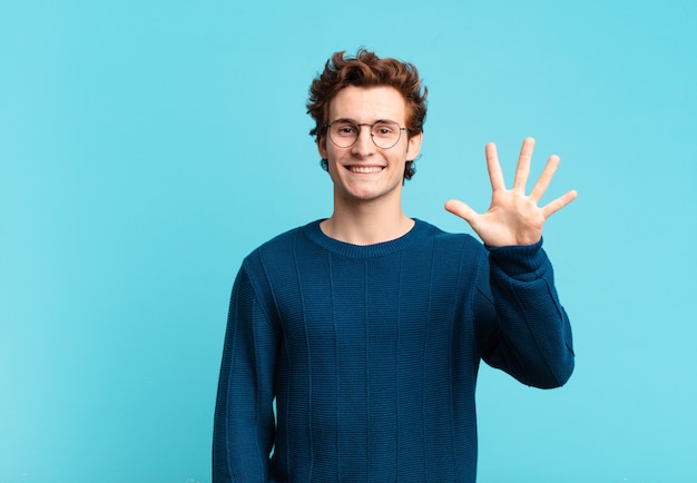 Jeune beau garçon souriant et à l'air sympathique, montrant le numéro cinq ou cinquième avec la main vers l'avant, compte à rebours