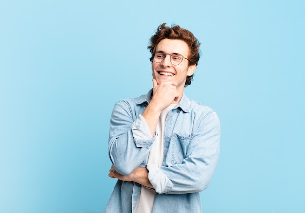 Jeune beau garçon souriant avec une expression heureuse et confiante avec la main sur le menton, se demandant et regardant sur le côté