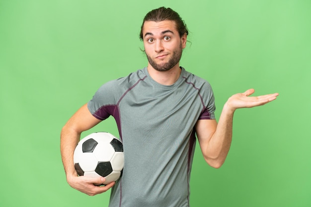 Jeune beau joueur de football homme sur fond isolé ayant des doutes tout en levant les mains