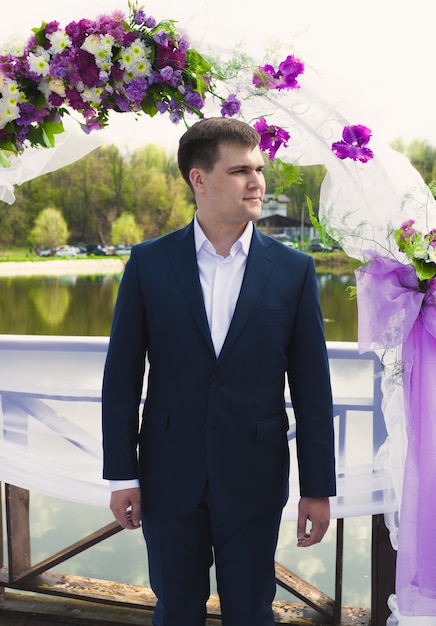 Jeune beau marié attendant la mariée sous l'arche florale lors de la cérémonie