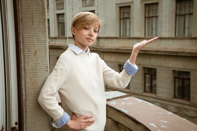 Jeune beau mec blond en pull beige posant sur le balcon