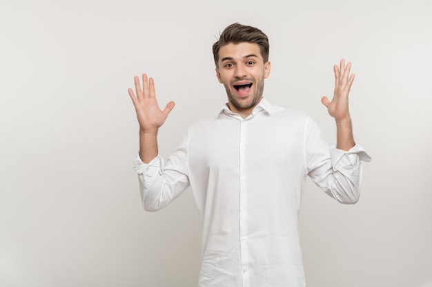 Un jeune beau mec étonné portant une chemise décontractée blanche à l'air choqué et gagnant