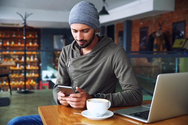 Jeune beau mec hipster au restaurant à l'aide d'un téléphone portable