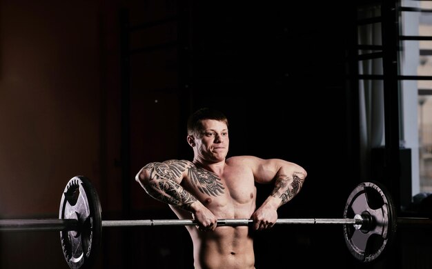 Jeune beau mec avec un torse nu faisant des exercices dans la salle de gym