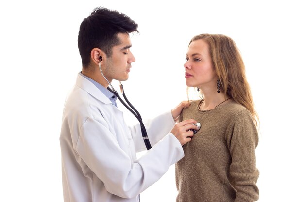 Jeune beau médecin en robe avec stéthoscope écoutant les battements de coeur d'une jeune jolie femme