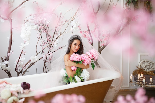 Jeune beau modèle assis dans une baignoire et tenant un bouquet de fleurs tout en regardant la caméra Photo de haute qualité