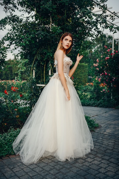 Jeune beau modèle pose dans une longue robe ivoire dans le jardin avec une couronne sur la tête