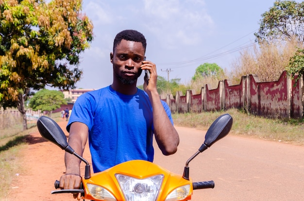 Jeune beau motard africain faisant des appels en attendant que son client arrive