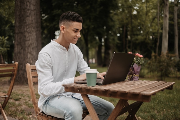 Jeune beau pigiste travaillant à distance sur un ordinateur portable. Homme heureux dans un parc informatique, faisant son travail à distance.