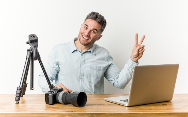 Jeune beau professeur de photographie joyeux et insouciant montrant un symbole de paix avec les doigts.