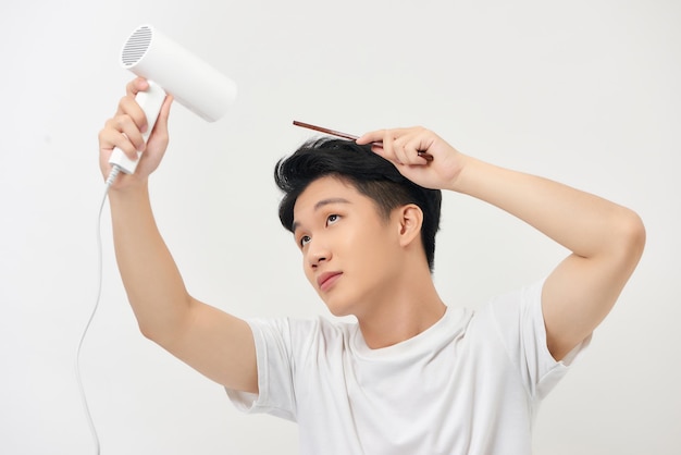 Jeune beau séchant ses cheveux isolé sur blanc