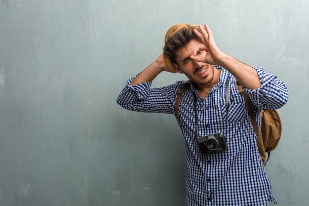 Jeune beau voyageur portant un chapeau de paille, un sac à dos et un appareil photo gai et confiant, faisant un geste ok, excité et hurlant, concept d&#39;approbation et de réussite