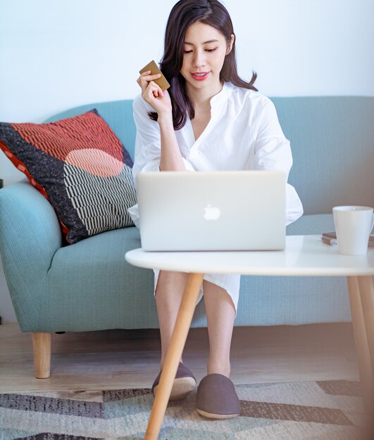 Jeune beauté asiatique faisant ses courses en ligne avec carte de crédit et ordinateur portable à la maison