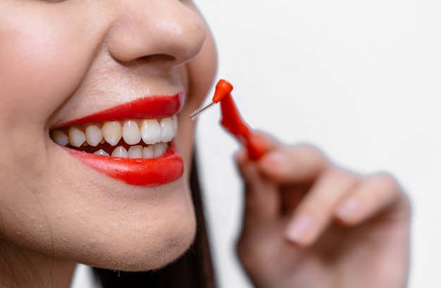 Jeune beauté aux lèvres rouges et aux dents parfaites tenant la brosse interdentaire des dents. Photo recadrée.