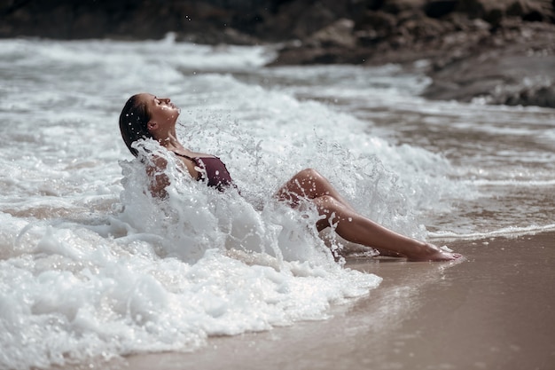 Une jeune beauté bronzée baigne dans les vagues et ferme les yeux.