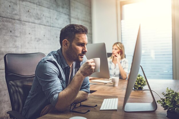 Jeune bel entrepreneur pensif sérieux travaillant sur ordinateur au bureau.