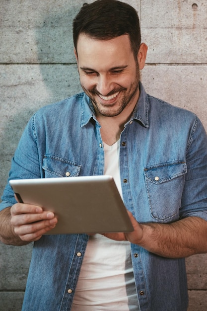 Jeune bel entrepreneur prospère regardant sur sa tablette, vérifiant les plans avant de commencer à travailler sur le chantier de construction.