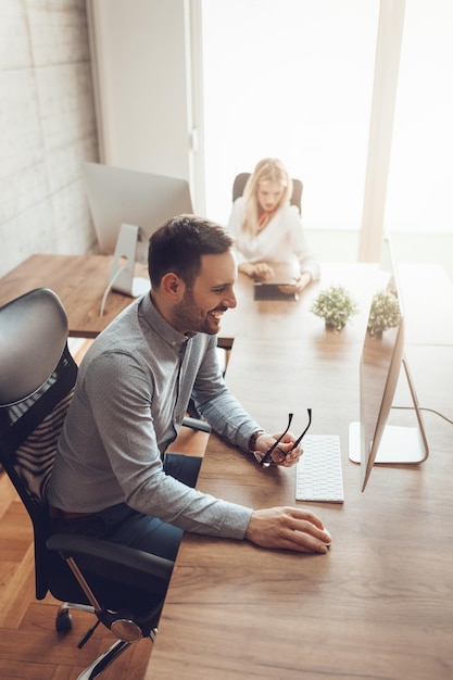 Jeune bel entrepreneur prospère travaillant sur ordinateur au bureau.