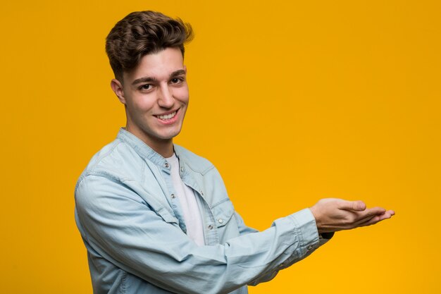 Jeune bel étudiant vêtu d'une chemise en jean tenant un espace de copie sur une paume.