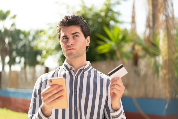 Jeune bel homme achetant avec le mobile avec une carte de crédit en pensant