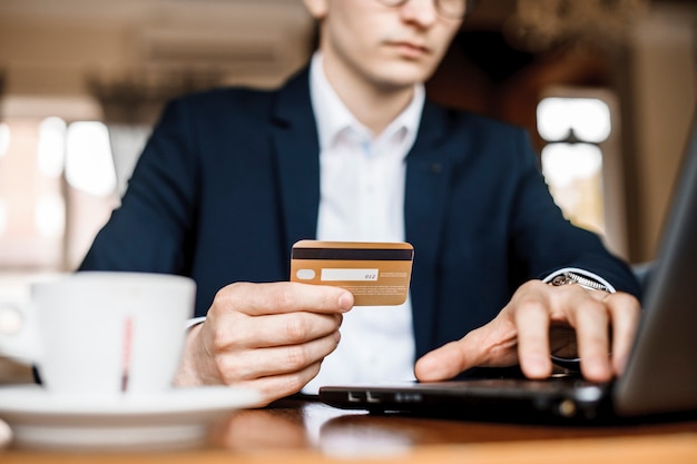 Jeune bel homme achète en ligne en utilisant une carte de crédit et un ordinateur portable dans un beau restaurant.