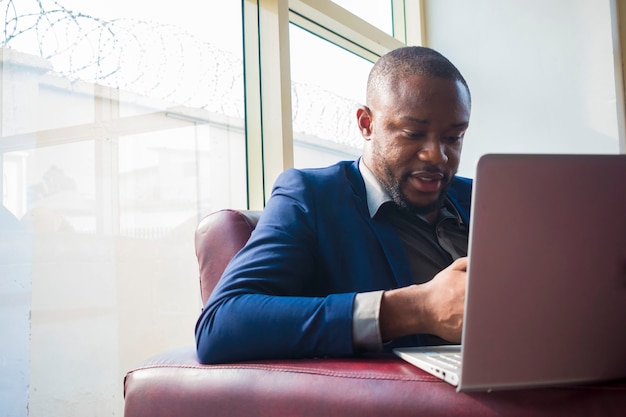Jeune bel homme d'affaires africain se sentant enthousiasmé par ce qu'il fait sur son ordinateur portable