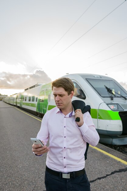 Jeune bel homme d'affaires à l'aide de téléphone mobile en face du train à la gare