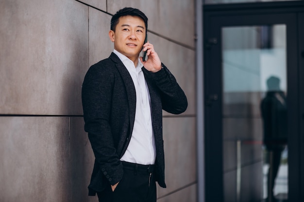 Jeune bel homme d'affaires asiatique en costume noir à l'aide de téléphone