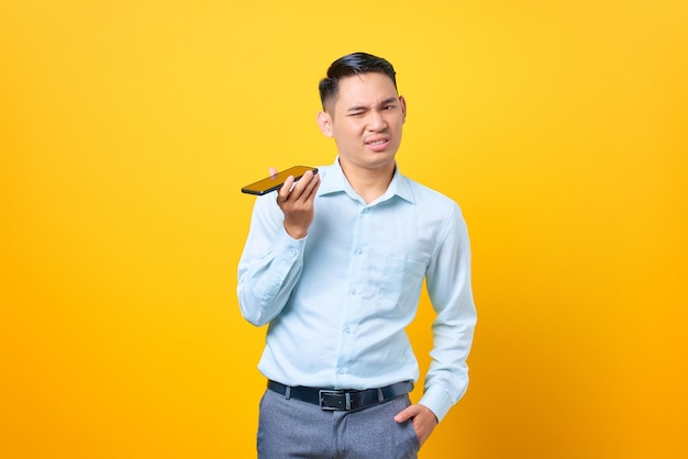 Jeune bel homme d'affaires confus parlant sur un smartphone sur fond jaune