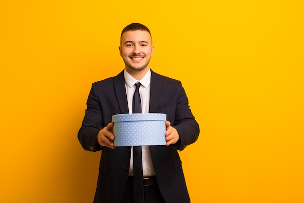 Jeune bel homme d'affaires contre un mur plat avec une boîte-cadeau