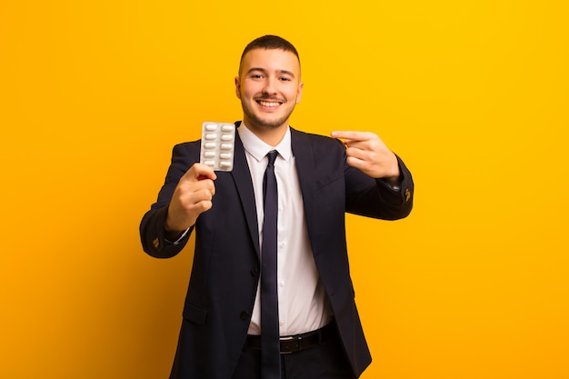 Jeune bel homme d'affaires contre un mur plat avec des capsules de pilules